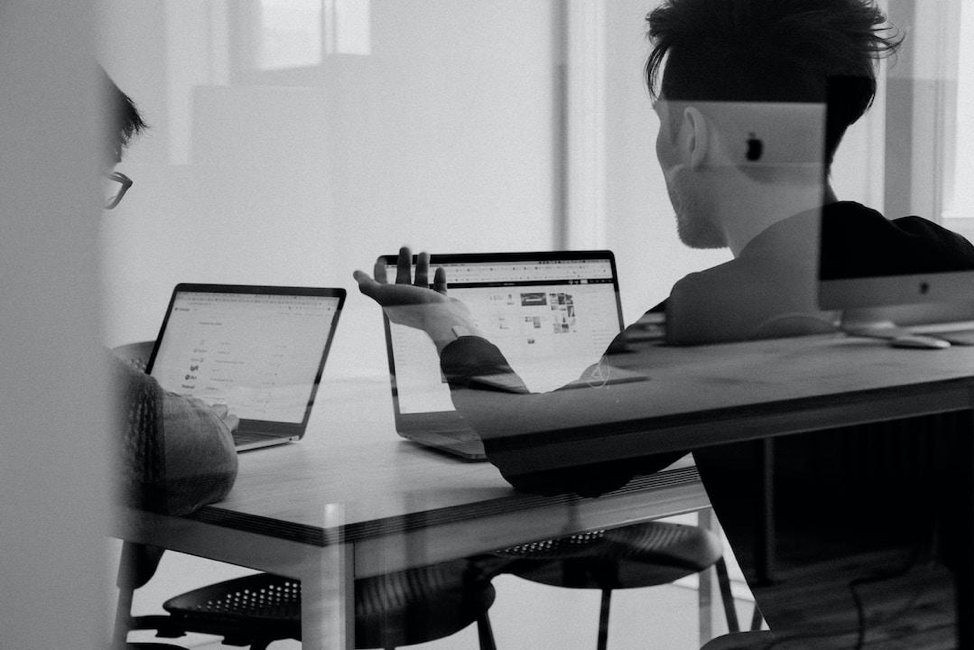 Two people sitting at a table with their laptops discussing the data from a parallel coordinate plot.